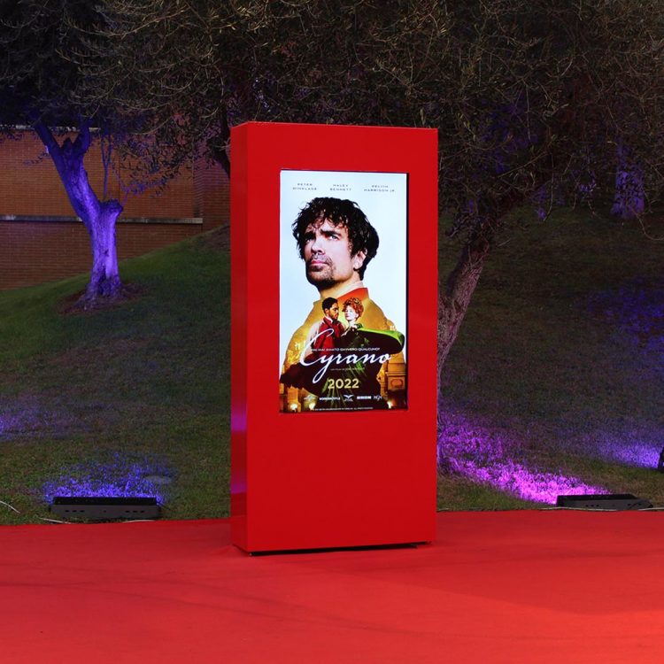 Totem rosso con Monitor LCD da 65 pollici incastonato, con manifesto digitale del film Cyrano.